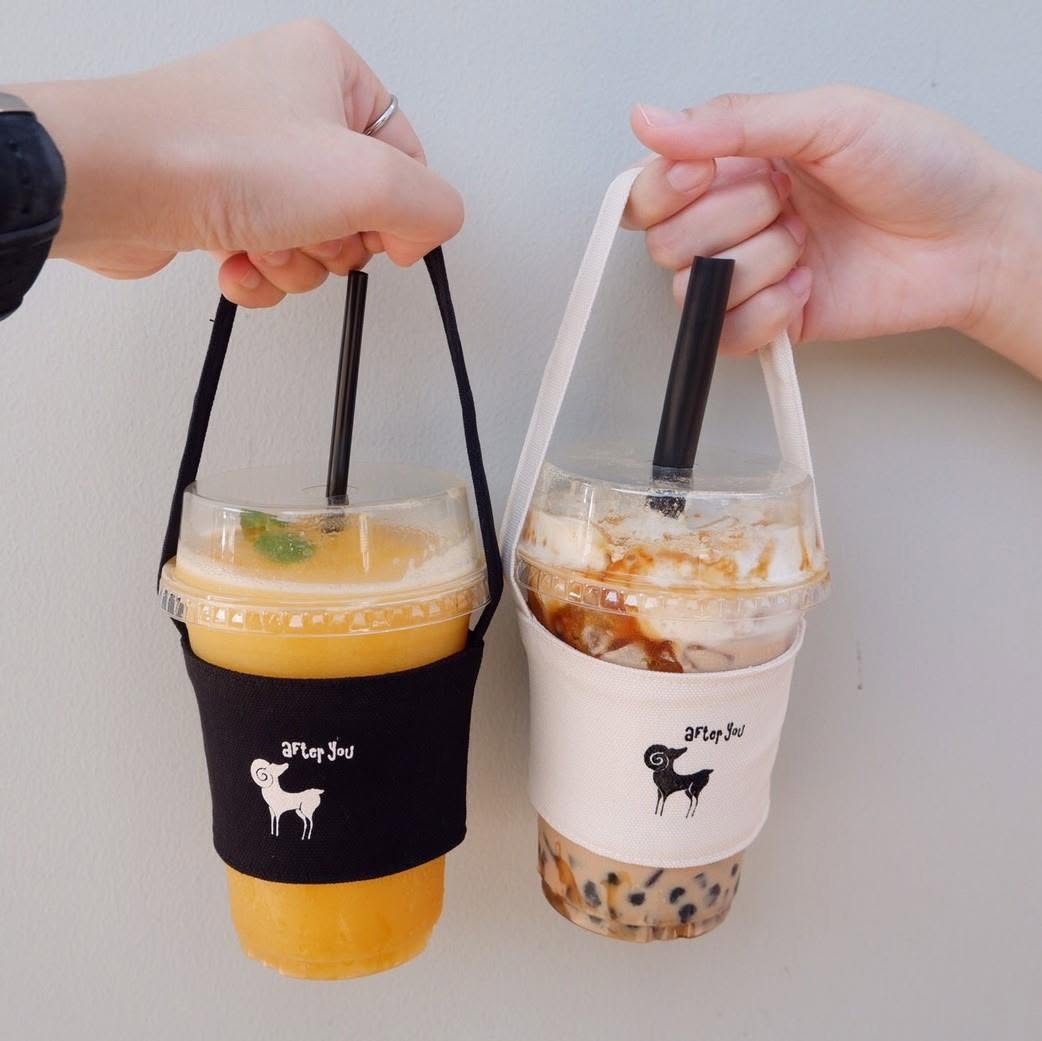 two iced drinks carried by hand in reusable canvas cup holders